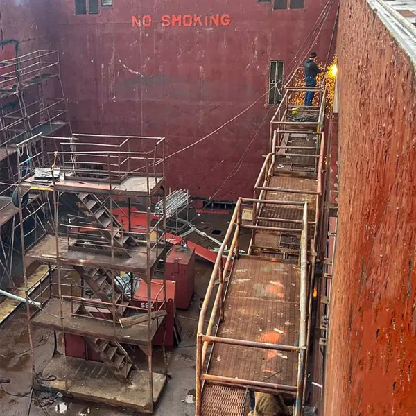 Ship repair team carrying out hull-side steel work from staging during dry dock support