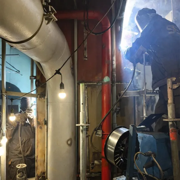 Onboard repair team with welders carrying out welding works inside a vessel engine room