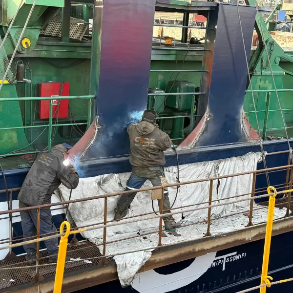 Ship repair team with welders carrying out steel welding works along the vessel side