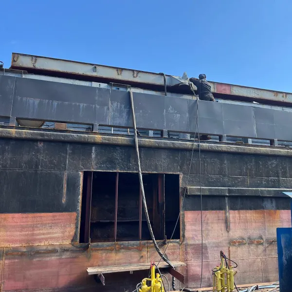 Steel worker carrying out hull steel repair on the side structure of a vessel