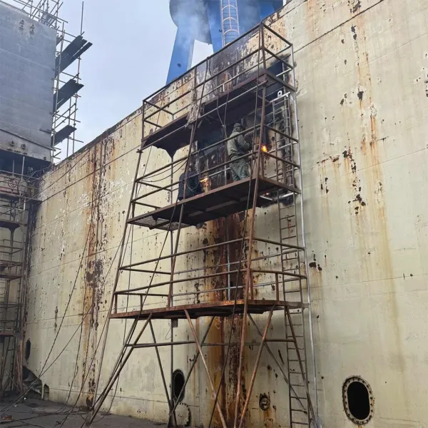 Steel worker carrying out hull side steel repair from staging during dry dock support