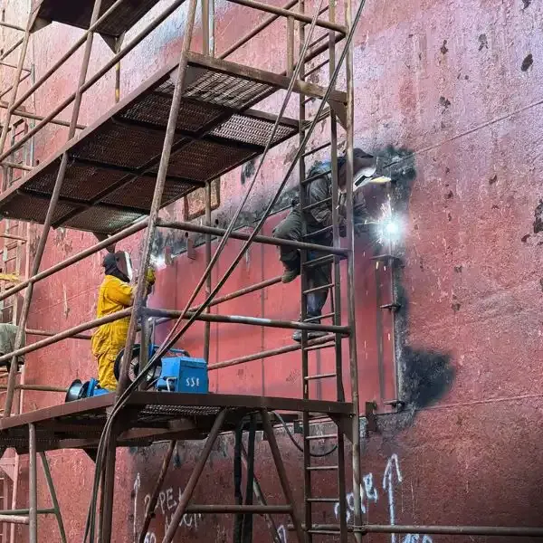 Certified Welders performing ship hull plate welding from scaffolding during dry dock repairs