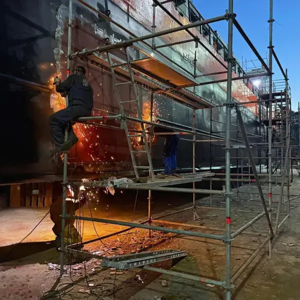 Ship repair workers carrying out hull steel hot work from scaffolding during dry dock repair