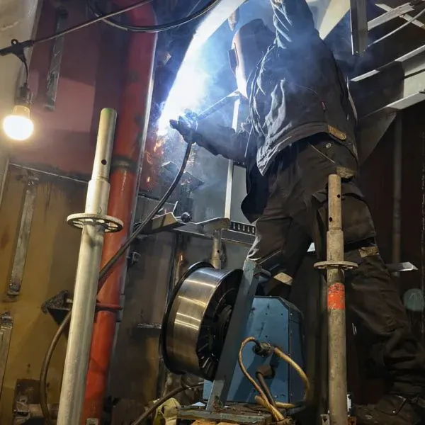 Welder carrying out onboard ship welding repair on steel structure with scaffold access during dry dock support works.