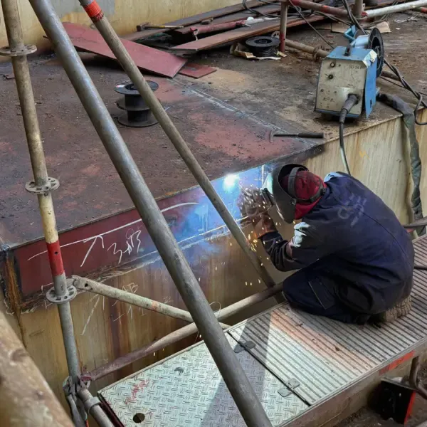Welder carrying out steel welding repair on ship structure with scaffold access during dry dock ship repair.